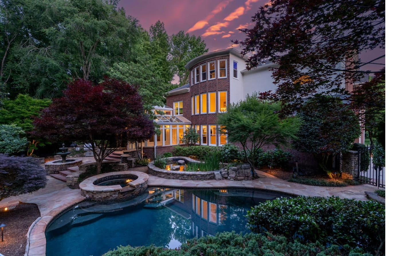 Rear twilight view of The Whitney Sanctuary with landscape lighting illuminating gardens and specimen trees
